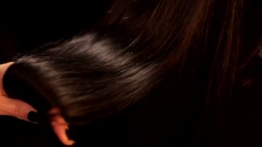 Kadın elinin siyah arkaplan çekimini kapat. Güzel düz, parlak, esmer, koyu renk saçları var.