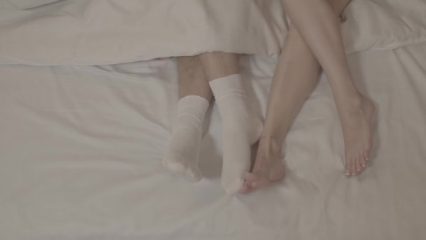 两个赤脚躺在床上的女人 在盖着白床单的毛毯下摸着穿着白袜子的男人的腿 — 图库视频影像