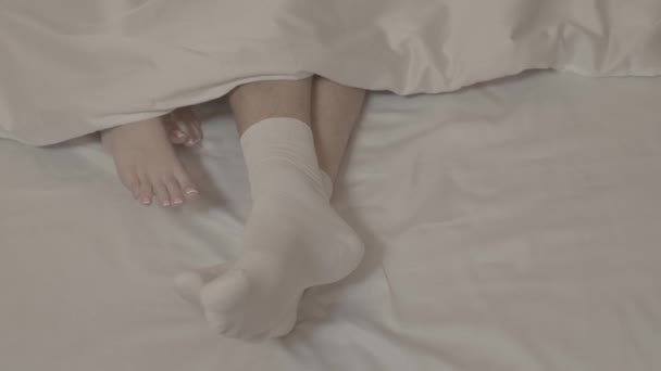 两个赤脚躺在床上的女人 在盖着毯子的白色被单上摸着穿着白袜的男人的腿 — 图库视频影像