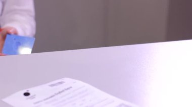 Kadın kasiyer erkek, yakın plan çekimde beyaz zemin üzerinde a4 sayfa kağıt başvuru formu ve plastik kart alışverişi yapıyor.