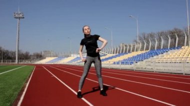 Genç çekici fit aktif bayan sporcu kaslarını ısıtıyor güneşli bir günde büyük stadyumun dışında çalışıyor.