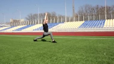 Genç, çekici, aktif, çömelme hareketleri yapan sporcu bir bayan. Büyük stadyumun dışında egzersiz yaparak kaslarını ısıtıyor.