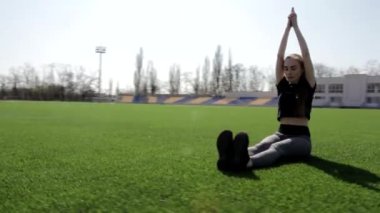 Çekici ve aktif bir kadın, sıcak ve güneşli bir günde sakin bir şekilde meditasyon yapan yeşil çimenlerin üzerinde yoga pozu veriyor.