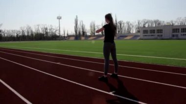 Genç, çekici, aktif, çömelme hareketleri yapan sporcu bir bayan. Büyük stadyumun dışında egzersiz yaparak kaslarını ısıtıyor.