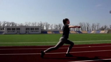 Aktif formda, çekici bir genç kız yürüyüşü, ısınma egzersizleri yapıyor. Dışarıda, büyük stadyumda egzersiz yapıyor.