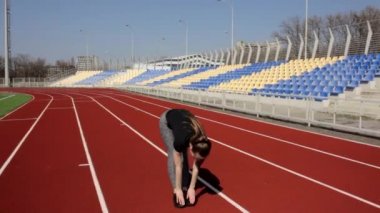 Güzel görünümlü genç kız spor yapıyor. Büyük stadyumdaki kasları ısıtmak için bacak esnetme egzersizi yapıyor.