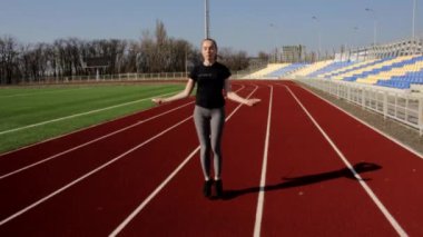 Genç çekici fit atletik kız ip atlıyor. Büyük stadyumda ağır çekimde ısınıyor.