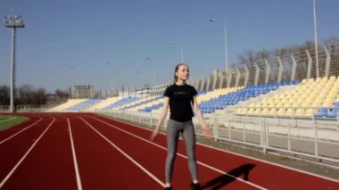 Genç, çekici, formda, atlayan atlet kız ağır çekimde güneşli bir günde büyük stadyumda kaslarını ısıtıyor.
