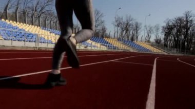 Genç atletik formda bir kadının koşu sahnesinin yavaş çekimleri. Güneşli bahar gününde açık havada büyük bir stadyum idmanı.