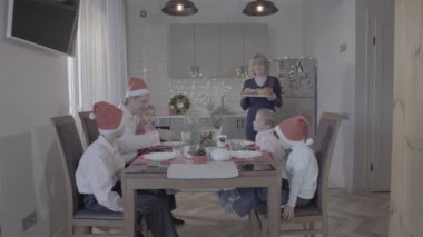 Mutlu dört çocuk, yeni yılı kutluyor. Mutfak masası, baba, oğul, anne yemeği servis ederken gülümsüyor.