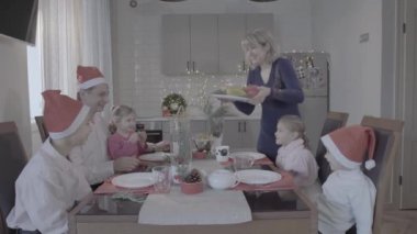 Heyecanlı altı kişilik aile Noel yemeğinin tadını çıkarsın Noel Baba şapkalı muhteşem sıcak mutfak kutlaması atmosferinde