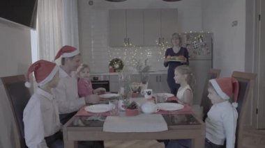 Heyecanlı altı kişilik güzel bir aile Noel yemeğinin tadını çıkarıyor. Kutlama atmosferinde. Noel Baba şapkalı harika bir mutfak.
