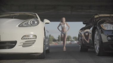 İki yeni spor yarış modern arabasının yakın plan çekimi. Arka planda çekici, seksi ve formda bir kadınla başlamaya hazır.