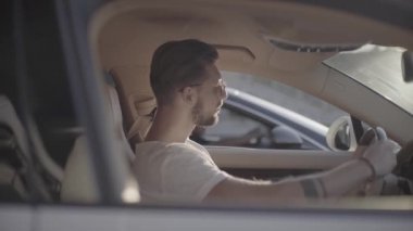 Güneş gözlüklü yakışıklı genç adam lüks spor yarış arabasında oturuyor rakibinin karşısında başlamaya hazır.