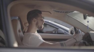 Güneş gözlüklü yakışıklı genç adam lüks spor yarış arabasında oturuyor rakibinin karşısında başlamaya hazır.