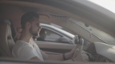 Çekici, genç, güneş gözlüklü yakışıklı adam lüks spor bir yarış arabasında rakibinin karşısında oturmaya hazır.