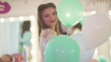 Genç ve çekici sarışın kadın parti atmosferinin tadını çıkartıyor. Elinde balonlarla etrafta gülümsüyor.
