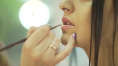 Profesyonel kadın makyaj sanatçısı ruj sürme fırçasıyla çekici genç model dudaklar boyuyor.