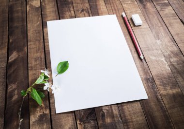 Fotoğraf boş örneği: antetli kağıt, kalem, silgi, kiraz çiçekleri ve yeşil yaprakları üzerinde ahşap arka plan. Duyarlı tasarım mockup.