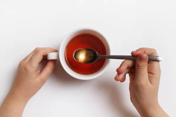 Baby hands with cup of tea and spoon on white background. Tea time.