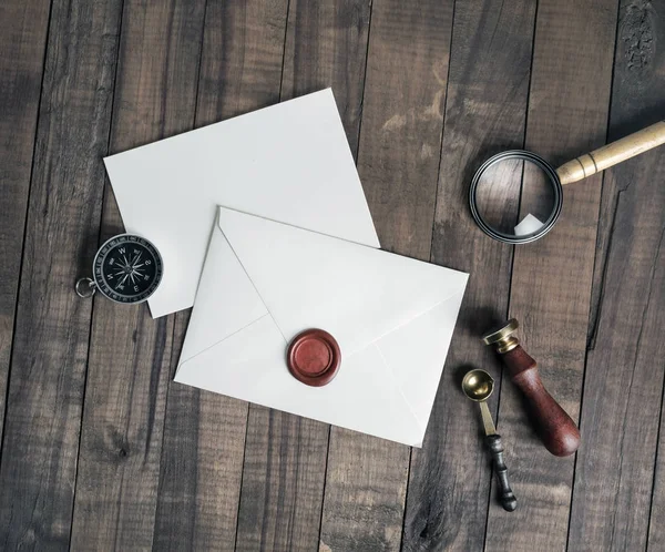 Blank envelope and stationery: wax seal, stamp, spoon, magnifier, compass and postcard on wooden background. Flat lay.