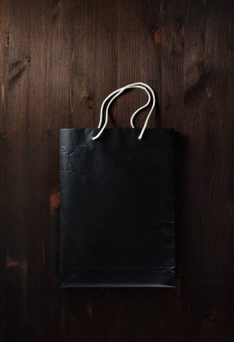 Boş siyah Kağıt alışveriş çantası beyaz iple ahşap arka plan üzerinde işler. Düz yatıyordu.