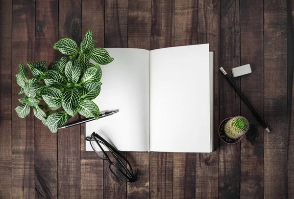 Blank open book, stationery and plants on wooden background. Flat lay.