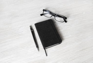 Boş siyah defter, açık tahta masa arka planında gözlük ve kalem. Markalaşma tasarımı için şablon.
