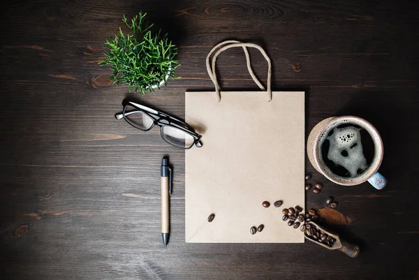 Kraft paper bag, coffee cup, coffee beans, glasses, pen and plant on wooden background. Top view. Flat lay.