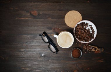 Kahve fincanı, kavrulmuş kahve çekirdekleri, kahve fincanı, bira altlığı ve tahta masa zemininde bardaklar. Düz yatıyordu.