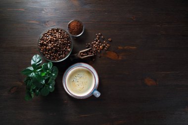 Lezzetli taze kahve. Kahve fincanı, kahve çekirdekleri, eski ahşap masa arka planında bitki ve toprak tozu. Üst Manzara. Düz yatıyordu.