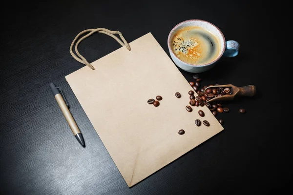 Foto Von Leerer Kraftpapiertüte Kaffeetasse Stift Und Kaffeebohnen Auf Schwarzem — Stockfoto