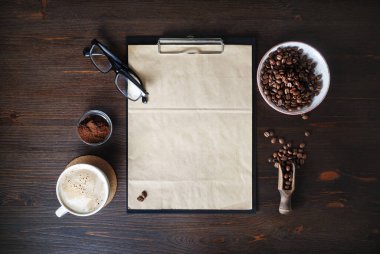 Kırtasiye seti ve kahve. Tahtada boş kese kağıdı, kahve fincanı, kahve çekirdekleri, bardaklar ve tahta zemin tozu var. Düz yatıyordu.