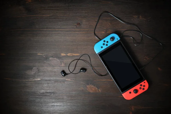 Minsk, Belarus - 7 Mayıs 2020: Nintendo oyun konsolu üzerinde siyah ekran ve ahşap masa arkasında parlak Joy-Con kontrolörleri var. Uzayı metin için kopyala. Üst Manzara. Düz yatıyordu.