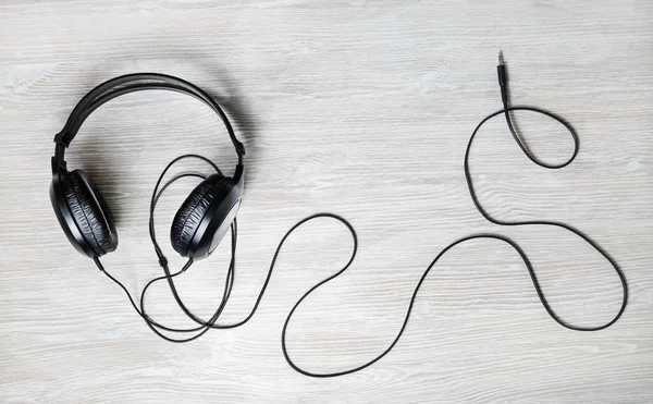 Black acoustic headphones on light wood table background. Top view. Flat lay.