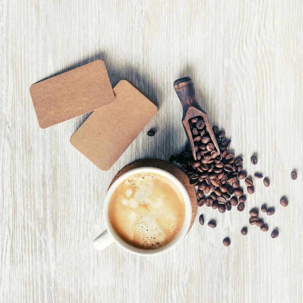 Blank vintage business cards, coffee cup and coffee beans on light wooden background. Top view. Flat lay.