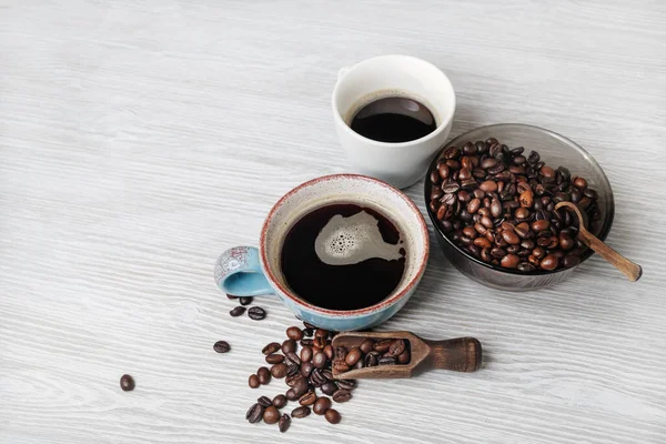 Delicious fresh coffee. Coffee cups and roasted coffee beans on light wood table background.
