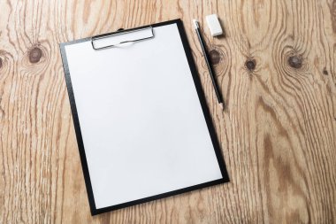 Ahşap masa zemininde boş kağıt, kalem ve silgi olan bir pano. Metnin için boşluk kopyala.