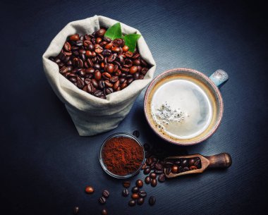 Taze, lezzetli kahve. Kahve fincanı, kavrulmuş kahve çekirdekleri ve arka planda siyah mutfak masası tozları..