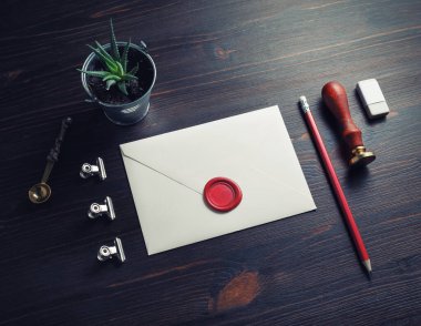 Retro posta kırtasiyesi. İçinde balmumu mühür, mühür, kalem, silgi, tahta arka planda bitki ve kaşık olan boş bir zarf..