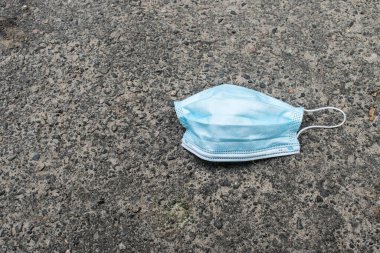 Kullanılmış bir tıbbi yüz maskesi bir parktaki şehir yolunun sağındaki asfaltta yatıyor. Koronavirüs salgını sırasında çevresel kirlilik ve atıklar.