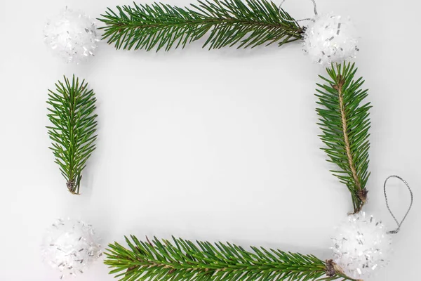 Creative layout for a Christmas card in the form of a square on a white background made of spruce branches and Christmas balls