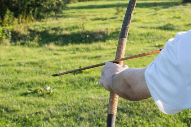 Güçlü erkek eller ok ve ok atmak için yay tutuyor. Okçuluk ile açık hava aktiviteleri