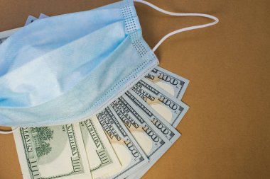 Soldaki kahverengi arka planda üzerinde tıbbi maske olan dolar hayranı var. Karantina ve salgın sırasında iş kavramı