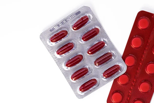 the silver package contains red tablets in the form of capsules next to a red package of tablets on a white background. The concept of prevention and care for your health