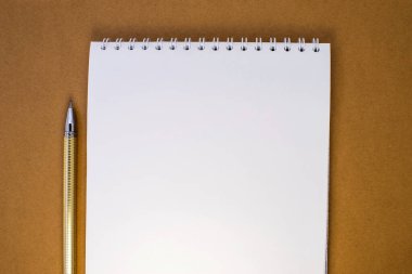 Kahverengi arka planda yanında sarı kalem olan beyaz boş bir defter var..