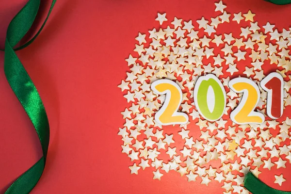 on the right on a red background among confetti in the form of yellow stars multi-colored numbers of 2021 framed by a green ribbon. Layout of Christmas and new year greeting cards