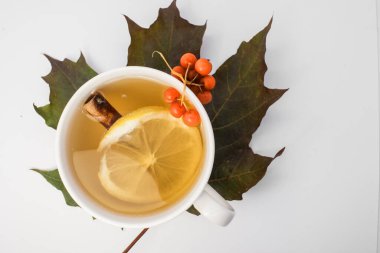 Büyük bir akçaağaç yaprağının üzerinde beyaz bir fincan çay var. Bir kase tarçın, limon ve Rowan 'da.