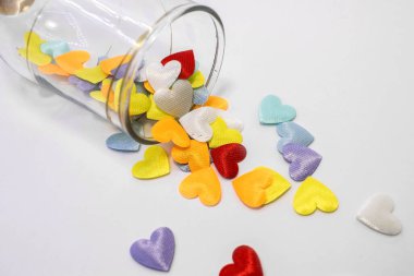 Beyaz arka planda saydam bir camdan çok renkli kalpler dökülüyor. Sol üst köşesinde kalpler olan cam.