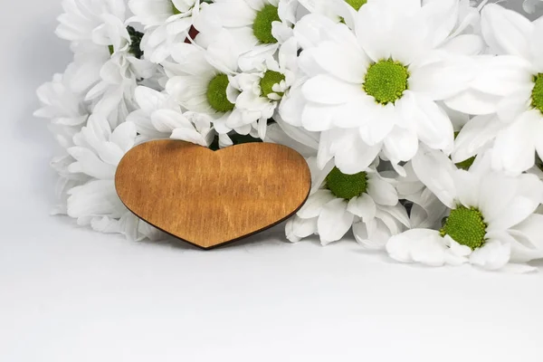 wooden heart on a light background among white chrysanthemum flowers. Delicate background for the holiday